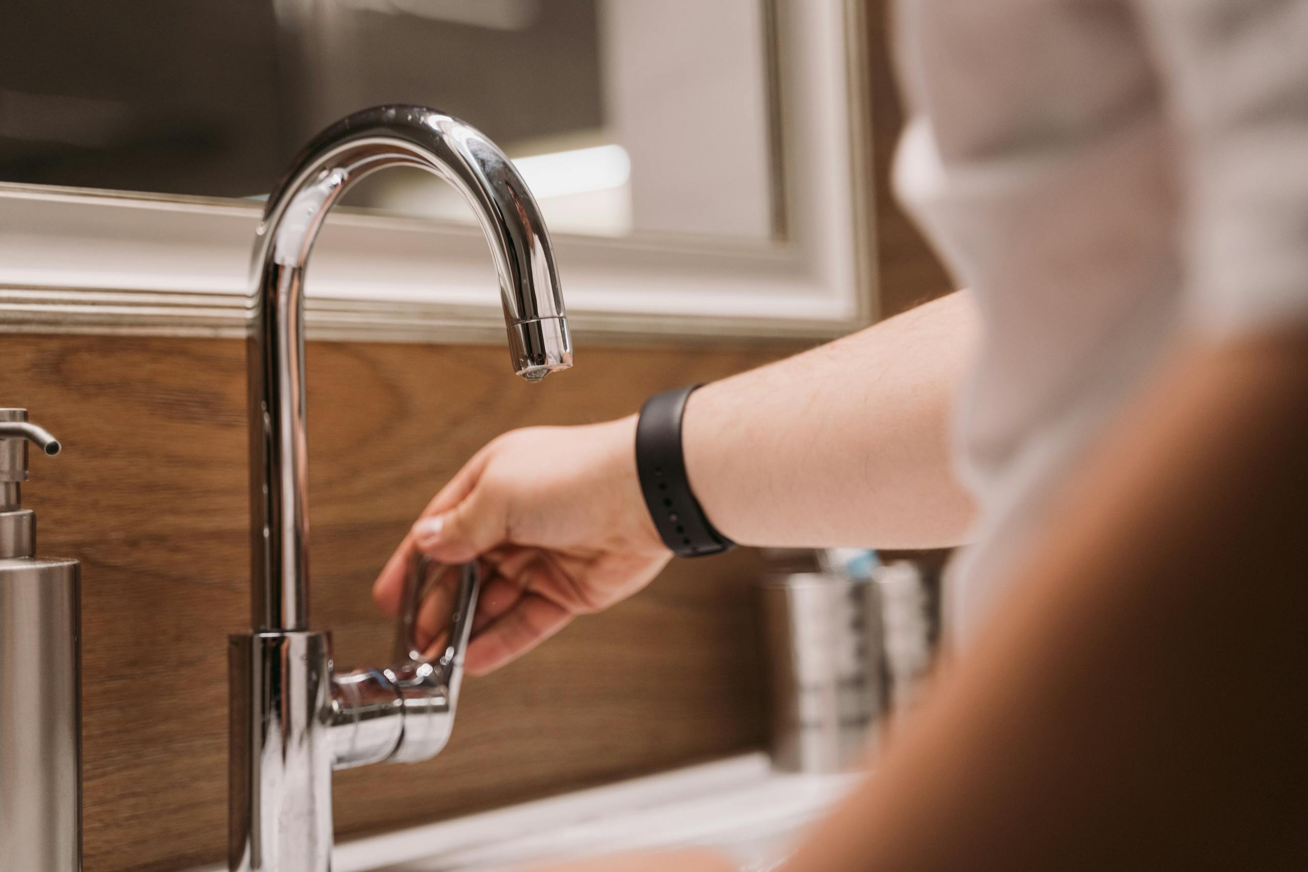 Close-up of a person's hand turning a chrome faucet handle in a modern bathroom setting.